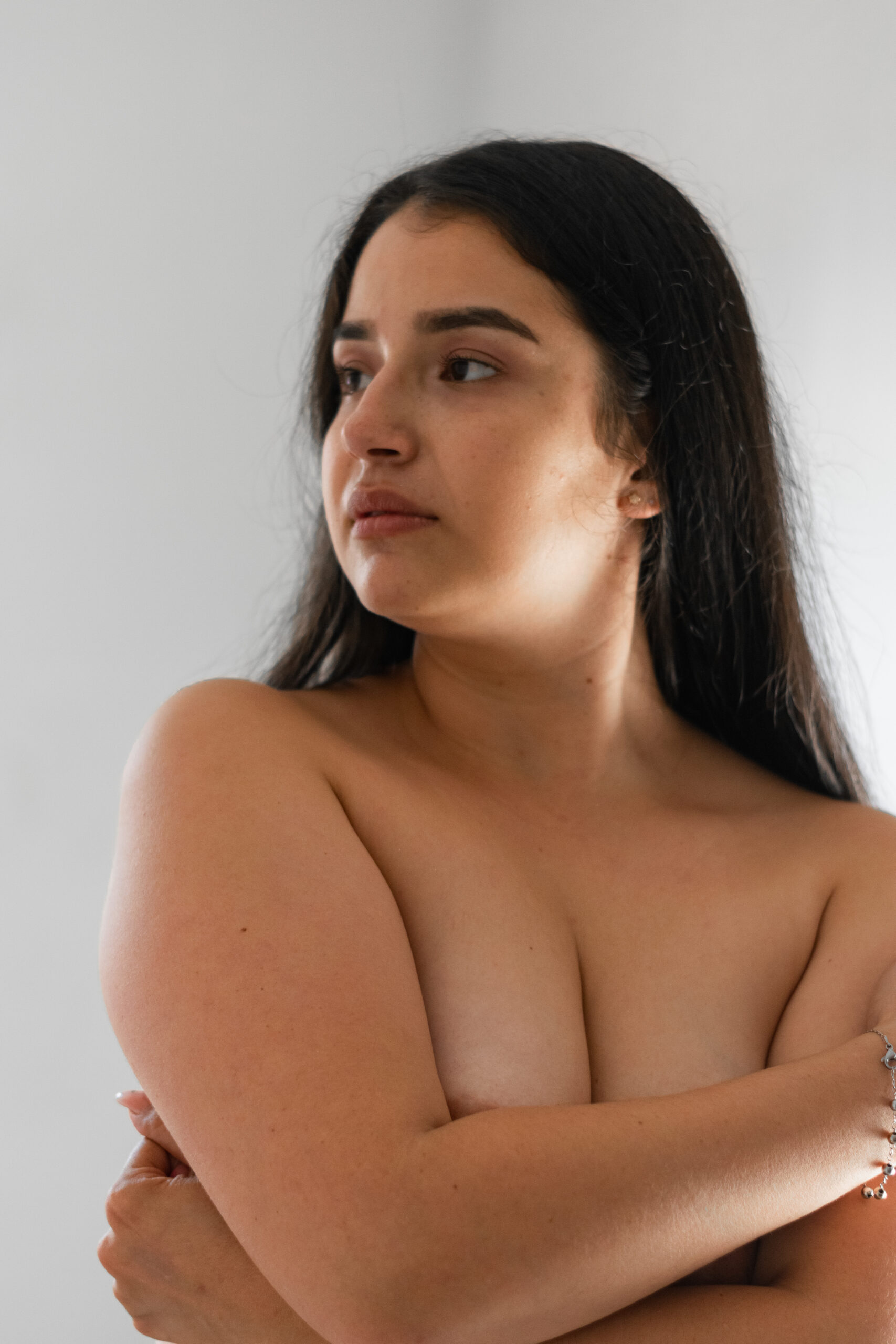 latina woman covering her breasts with her hands while looking to the side, on a white background